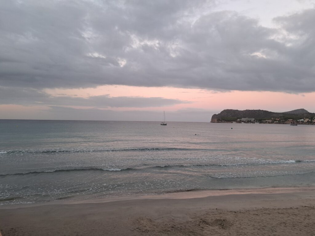 Takový útulný západ slunce, který vybravil oblohu do pastelově růžového tónu, celé to působí takovým uklidňujícím dojmem. Na fotce je vidět akorát klidné moře, na něm jedna plachetnice a v pravém zadním rohu skála. Obloha je plná mraků.