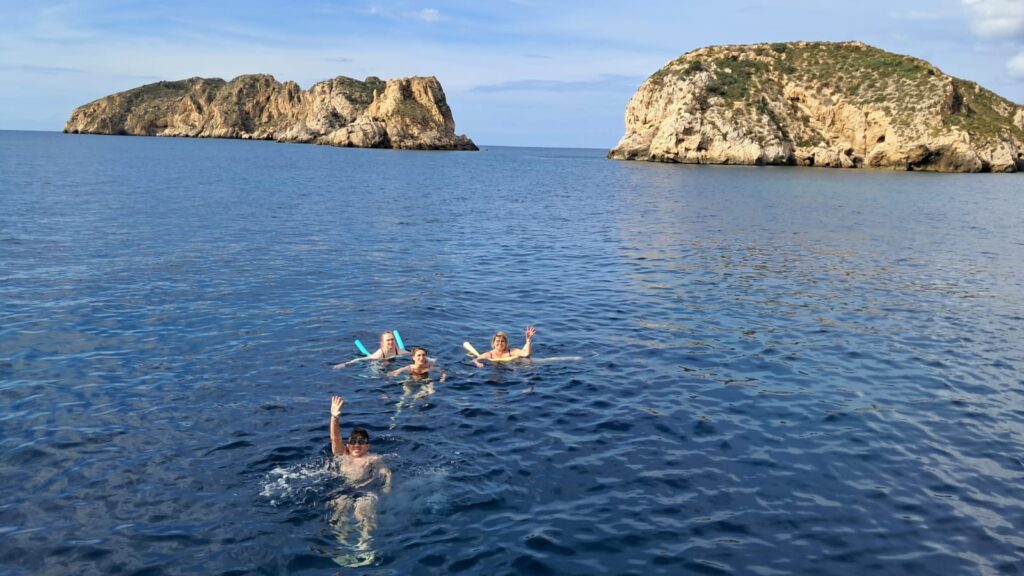 Koupačka na otevřeném moři na výletu lodí. Skvělý výlet, 2 účastníci a 2 průvodci byli zachycení ve vodě, fotka je uplně ikonická, za nimi se tyčí dvě velké skály v moři, voda je sytě modrá